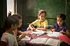 Four young girls are sitting together at a table, coloring books.