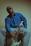 Artist Nsikak David poses behind a green background while holding his guitar