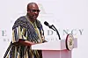 The President of Ghana, John Mahama, stands at a podium, speaking into a mic, wearing a traditional garment known as a fugu.