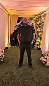 DJ Stretch is standing in a floral wedding setup under warm lights, dressed in black.