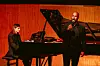 John Mburu performs with a clenched fist while an accompanist plays a grand piano on a stage.