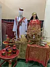 Two mannequins dressed in traditional jirtig attire and standing behind golden and red tables and trays carrying jirtig paraphernalia.