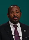 Abiy Ahmed Ali speaks into a microphone at COP28 in Dubai, wearing a suit and COP28 UAE lapel pin.