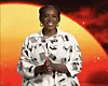 Wunmi Mosaku smiles in a golden background, hands clapped together.