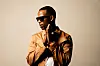 A press image of Zakes Bantwini. He looks to one side, wearing dark shades and a light brown jacket.