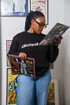 An image of Zee, OkayAfrica's social media reporter, wearing an OkayAfrica sweatshirt and holding two vinyls