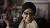 The late Winnie Mandela smiles while she gestures with her hand. She wears a black turban.