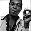 Fela Kuti, as photographed by Rick McGinnis in 1980. Kuti holds a cigarette while staring directly at the camera.