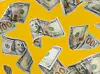 A photo of dollar notes raining against a bright yellow background.