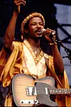 A younger King Sunny Ade performing with a guitar hanging from his shoulder in 1983.