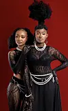 Gloria Munga (left) and Maggie Atieno (right) of We Are Nubia pose against a red background, wearing black lace outfits with pearl accessories and bold hairstyles.