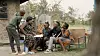 Several people sit and talk together in a yard outside a house in a still from the Kenyan documentary 'Widow Champion.'