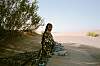 Dua Saleh is sitting in the shade of a bush in the desert, wearing a grey jalabiya and an elaborate green caftan.