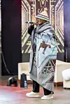 Wave Rhyder is holding a microphone onstage in a traditional Basotho-patterned blanket and hat.