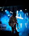Onesimus is silhouetted standing onstage under bright blue concert lights.