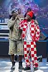 Chile One and Onesimus are singing onstage in front of a large LED display with concert equipment nearby.