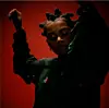 Joya Mooi is standing with arms raised in a dark outfit against a red background.