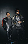 Blaqbonez and Asake are in black leather clothing and sunglasses, standing against a dark background.