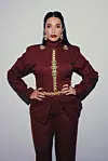 Inez is wearing a red Moroccan suit with large golden jewelry and looking directly into the camera.