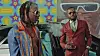 French-Ivorian artist Jeune Morty and another man are posing beside a classic car in front of a colorful mural and billboard.