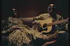 A promo picture for Amadou & Miriam’s documentary showing at Encounters Film Festival. Both are sitting on a couch. Amadou holds a guitar while Miriam relaxes next to him, her feet resting comfortably on his leg.
