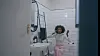 Woman sitting in a bathroom with white tiled walls and a sink nearby.