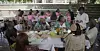 Group of people seated at a round table under a pavilion during an outdoor meal.