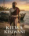 Man standing on a beach beside wooden fishing boats at sunset.