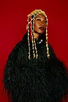 Studio portrait of Fatoumata Diawara in a black textured outfit and a beaded headpiece against a red background.