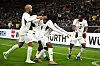 Ghana players in white celebrate a goal on the pitch during a match against Germany.