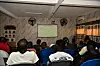 People seated in a room watch a soccer match on a wall-mounted television.