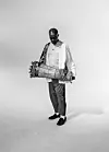 An image of Sola Akingbola holding a drum. He stands against a white background.