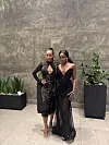 Christine Mosha (L)  stands next to Abigail Chams (R), both posing in black evening dresses.