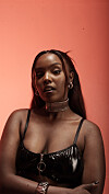 Studio portrait of Nikita Kering’ in a black shiny top against a coral background.