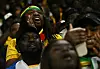 Ghana supporters in yellow and team colors react excitedly in the stands at Cardiff City Stadium.