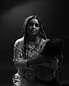 Black and white image of Neta holding a toddler in her arm while looking directly into the camera with a serious facial expression.