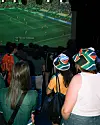 A crowd of fans watches a soccer game on a big screen in a packed setting.