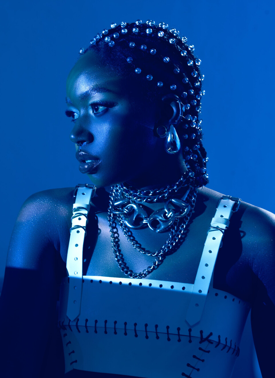 Blue-lit portrait of Karun wearing a studded headpiece and layered jewelry.