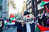 Protesters holding Sudan flags and a Free Sudan sign during a march on a city street.
