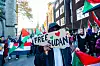 Protesters holding Sudan flags and a Free Sudan sign during a march on a city street.