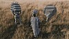 Muneyi stands between two masked figures; the three striped figures stand in tall grass in an open field.