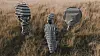 Muneyi stands between two masked figures; the three striped figures stand in tall grass in an open field.