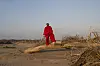 Muneyi stands atop a dead tree, dressed in red.