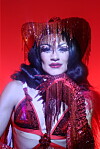 Ana Masreya, wearing a black wig and a pink cowboy hat, looks directly into the camera, her chin propped up on her hand, her hand in a pink glove.