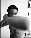 Black-and-white portrait of a shirtless boxer with one arm raised in front of the camera.