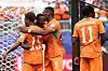Cote d'Ivoire players in orange kits celebrate near the goal after scoring in a World Cup match.
