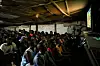 A crowd of Nigerian supporters watching a football match on a large screen in a dimly lit viewing center.