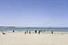 A beach with turquoise waters and a few people playing football on the sand.