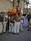 A man in orange clothes playing the qraqeb is jumping extremely high.