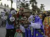 Two smiling men are holding large castanets and playing them, wearing colorful blue-and-green traditional Moroccan attire.